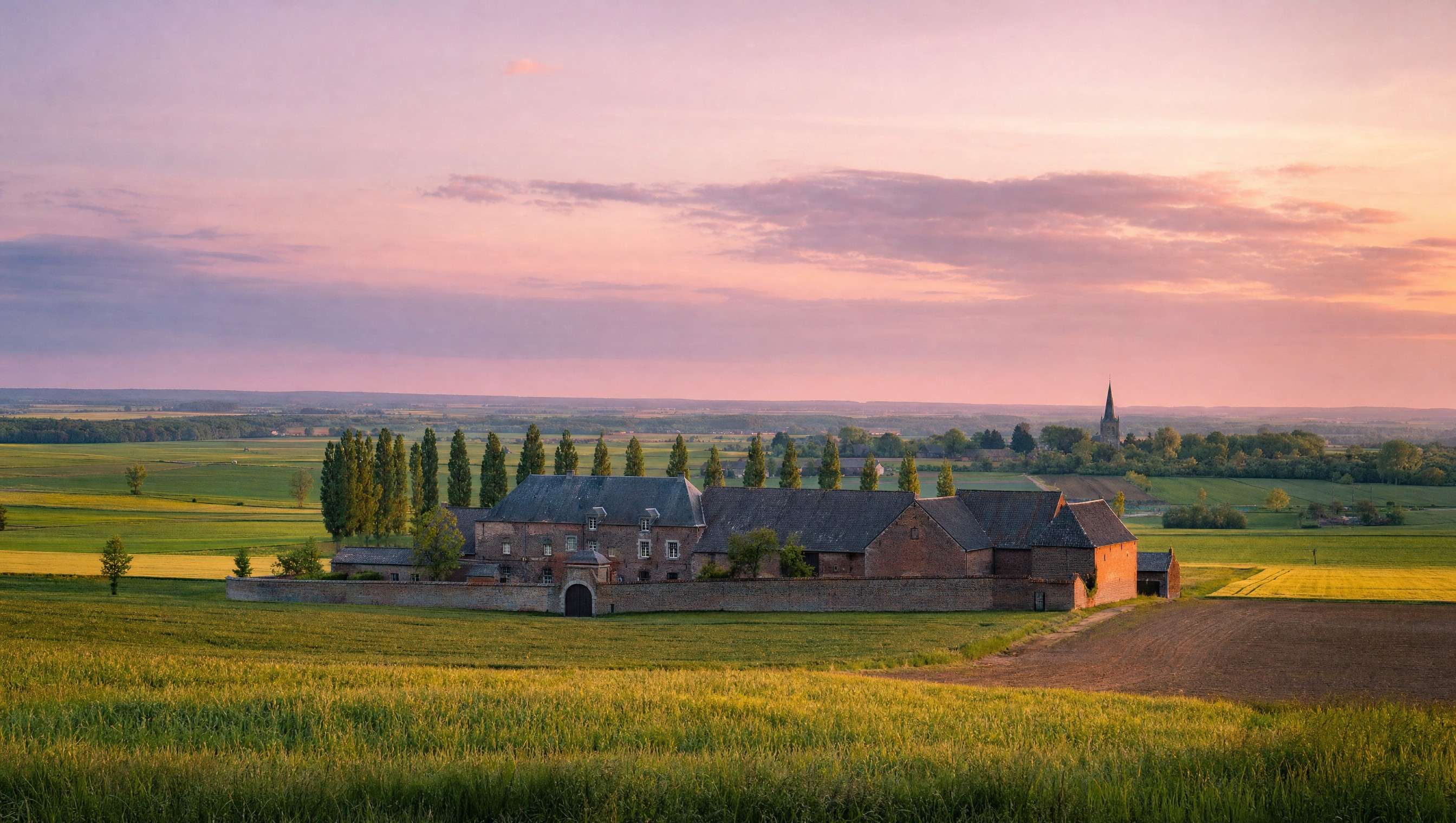 Campagne de Hesbaye au coucher du soleil, ferme en carré en briques et champs ouverts