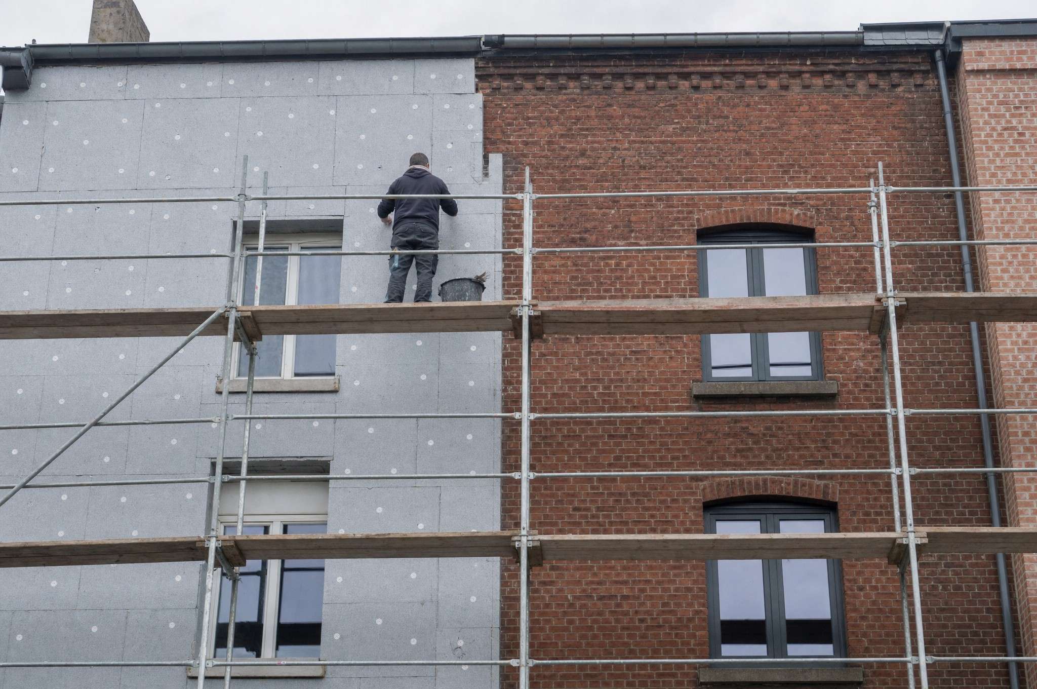 Façade en briques à moitié recouverte de panneaux isolants, échafaudage en place